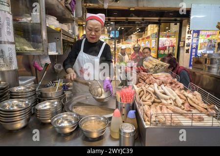 Un vendeur de rue prépare attentivement un plat au bord de la route avec une variété de viande sur l'affichage Banque D'Images