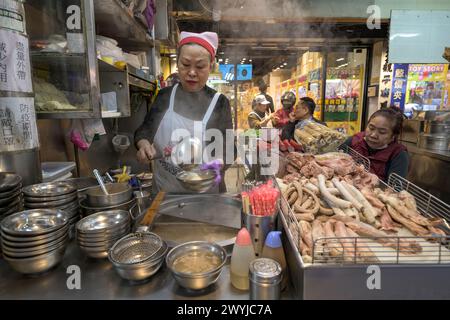 Un vendeur de rue prépare attentivement un plat au bord de la route avec une variété de viande sur l'affichage Banque D'Images