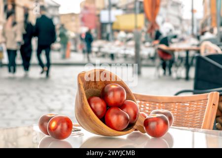 Plusieurs tomates cerises noires mûres avec une tasse en bois, macro, sur le fond d'un café de rue. Banque D'Images