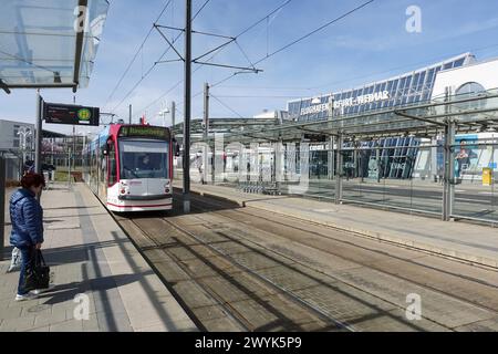 27.03.2024, Erfurt, Thueringen, GER - Strassenbahn der Linie 4 vor dem terminal des Flughafen Erfurt-Weimar. Alltag, aussen, Aussenaufnahme, Bahn, Befoerderung, deutsch, Deutschland, Erfurt, Europa, europaeisch, Fahrgast, Flughafen, Flughafen Erfurt-Weimar, Flughafengebaeude, Frau, Fruehjahr, Fruehling, Gebaeude, Gesellschaft, Individualverkehr, Jahreszeit, Linie 4, Mensch, Nahverkehr, oeffentlicher Personennahverkehr, OEPNV, Personenbefoerderung, Personentransport, Personenverkehr, QF, Querformat, Schiene, Schienenverkehr, Stadt, Stadtansicht, Stadtbahn, Stadtbild, Stadtverkehr, Stras Banque D'Images