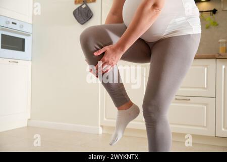 Fitness à la maison pendant la grossesse et problèmes avec une blessure à la jambe. Femme enceinte à l'entraînement sportif s'accroche à un genou meurtri, exercices à pr Banque D'Images