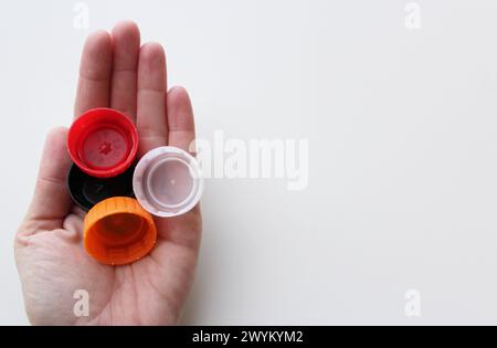 Main de femme tenant quatre couvercles en plastique sur fond blanc, espace pour la copie. Durabilité, concept de recyclage pour la Journée mondiale de l'environnement du 5 juin Banque D'Images