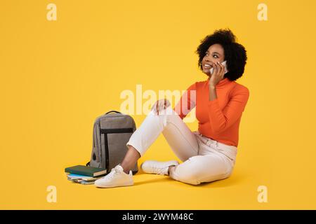 Jeune femme réfléchie avec des cheveux afro assis les jambes croisées, parlant au téléphone Banque D'Images