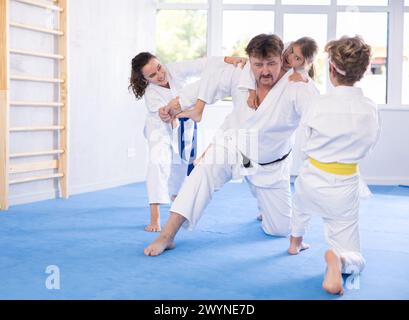 Cours de judo ou de JIU jitsu - famille avec deux enfants s'exerçant à saisir et à lancer sur des tapis de sport Banque D'Images