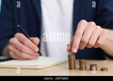 Économies financières. Homme empilant des pièces à la table en bois, gros plan Banque D'Images