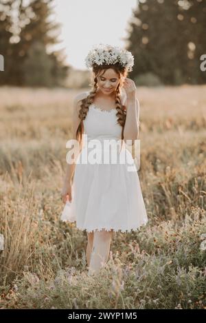 fille en robe blanche avec couronne à fleurs et tresses dans le style boho en été. Ajout d'une simulation de petit grain de la photographie de film Banque D'Images