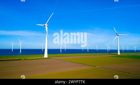 Un groupe de moulins à vent se dresse haut dans un champ à côté de l'océan, leurs lames tournant gracieusement dans la brise du printemps. éoliennes, énergie verte, jour de la terre Banque D'Images