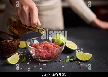 Femme verse l'huile d'olive de cuisson sur le filet de thon tranché et haché dans un bol en verre cuisant le tartare traditionnel Banque D'Images