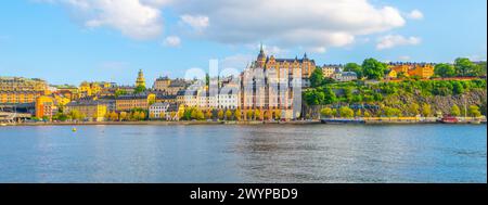 La lumière chaude du soleil baigne les bâtiments historiques le long du front de mer de Sodermalm, avec une végétation luxuriante accentuant le paysage urbain dynamique contre les eaux sereines. Stockholm, Suède Banque D'Images