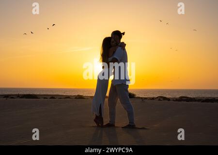 Jeune couple s'embrassant avec coucher de soleil en arrière-plan ayant un moment paisible d'intimité pendant les vacances Banque D'Images