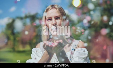 Une fille souffle des confettis en papier multicolores de ses mains. Banque D'Images