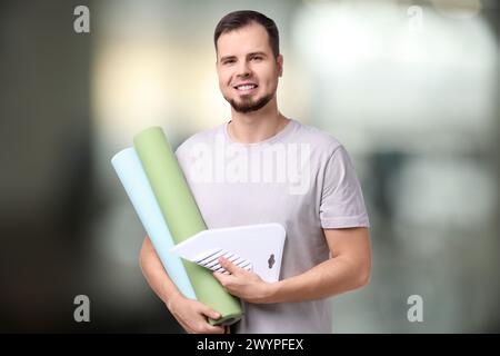 Homme avec des rouleaux de papier peint et outil de lissage sur fond flou Banque D'Images