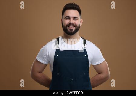 Homme souriant dans le tablier de cuisine sur fond brun. Maquette pour le design Banque D'Images