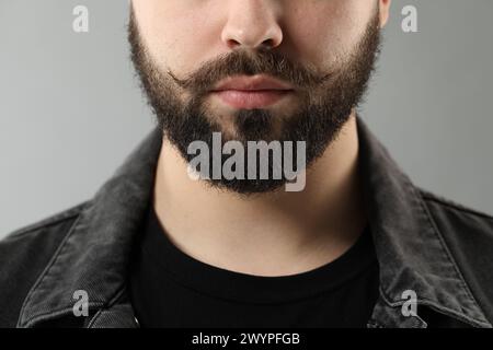 Beau jeune homme avec moustache sur fond gris, gros plan Banque D'Images