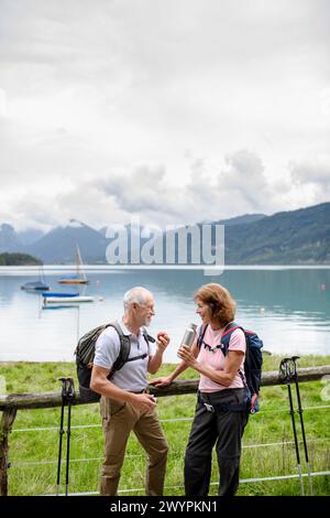 Couple de personnes âgées actives randonnant ensemble dans les montagnes. Boire du café et avoir une collation saine, pour obtenir de l'énergie. Touriste senior avec des sacs à dos au repos Banque D'Images