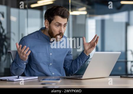 Photo d'un homme surpris dans un cadre de bureau, réagissant avec choc à quelque chose sur l'écran de son ordinateur portable. Capture le concept de nouvelles ou d'erreurs inattendues. Banque D'Images