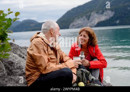 Couple de personnes âgées actives randonnant ensemble dans les montagnes. Boire du café et avoir une collation saine, pour obtenir de l'énergie. Touriste senior avec des sacs à dos au repos Banque D'Images