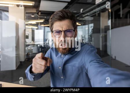 Un employé de bureau furieux gesticule tout en criant lors d'un appel téléphonique, montrant la frustration et le stress sur le lieu de travail dans un environnement de bureau moderne. Banque D'Images