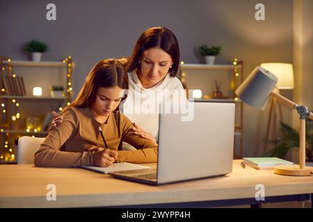 Mère et jeune fille wtitting tâche, lettre près de l'ordinateur portable, famille dans l'amour, maternité heureuse Banque D'Images