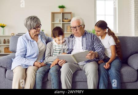 Grands-parents et enfants assis sur le canapé et lisant une histoire d'un livre pour enfants Banque D'Images