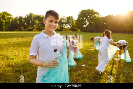 Adolescent souriant garçon avec sac poubelle collectant des ordures en plastique dans le parc d'été. Banque D'Images