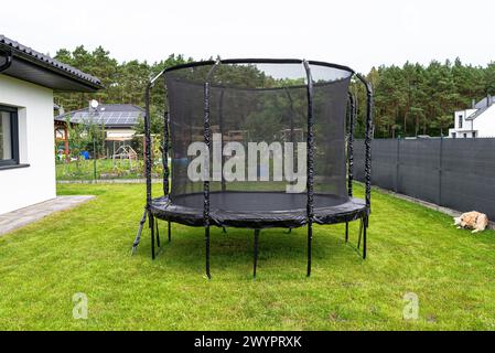 Grand trampoline de saut pour enfants avec filet de protection et fermeture éclair fermée, debout dans le jardin, chien Golden retriever visible. Banque D'Images