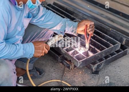 Le travailleur utilise une pince pour saisir le métal et souder la grille de drain en usine. Banque D'Images