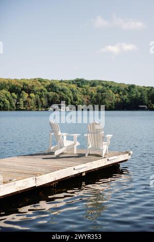 Sérénité au bord du lac avec deux chaises Adirondack blanches sur quai en bois Banque D'Images