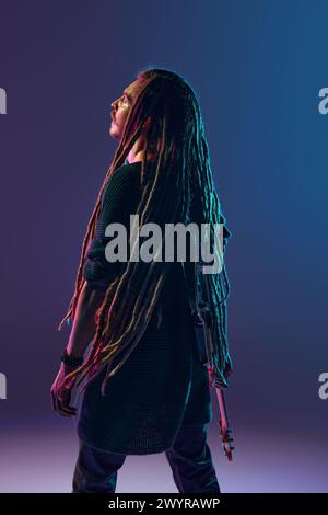 Portrait de guitariste talentueux avec des dreadlocks debout sur scène sur fond violet foncé dans la lumière néon. Musique pour âme Banque D'Images