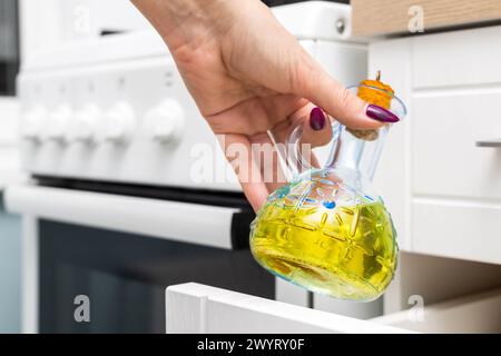 femme au foyer sort une bouteille en verre d'huile de tournesol de l'armoire de cuisine. bouteille en verre avec huile de cuisson. bouteille d'huile d'olive. homme tenant une bouteille de Banque D'Images