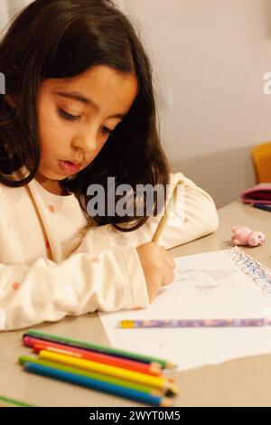 Concentrée fille peignant sur une feuille de papier avec ses crayons de couleur Banque D'Images