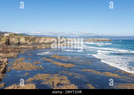 Littoral pittoresque, rivages rocheux, eaux bleues, vagues s'écrasant, ciel clair, montagnes lointaines, exploration paisible, environnement intact. Banque D'Images