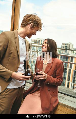 Un homme élégant se tient à côté d'une femme tenant gracieusement un verre de vin Banque D'Images