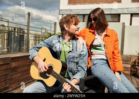 Un homme assis à côté d'une femme, sérénant avec une guitare tout en profitant du coucher de soleil ensemble Banque D'Images