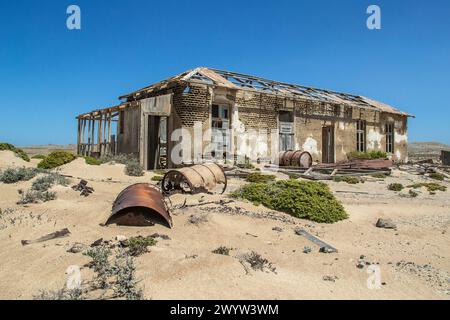 Barils de pétrole rouillés, sable et végétation désertique devant une maison de mineur abandonnée à Bogenfels, Namibie Banque D'Images