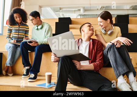 Groupe multiculturel de jeunes adultes assis sur un banc, engrossé dans des ordinateurs portables, collaborant à des missions éducatives. Banque D'Images