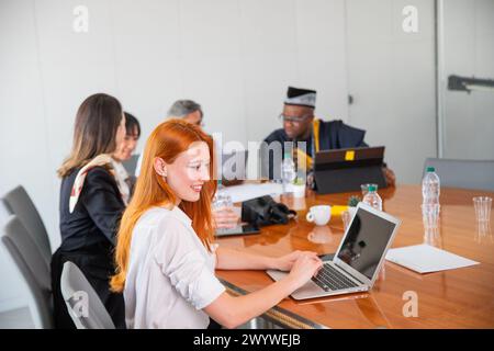 Une femme d'affaires utilise l'ordinateur portable lors d'une réunion d'entreprise, ses collègues travaillent en arrière-plan Banque D'Images