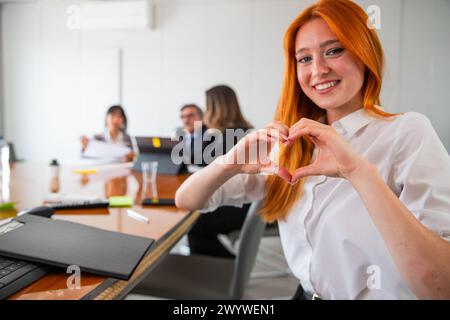 Une femme d'affaires montre un cœur lors d'une réunion d'affaires, concept de passion pour l'environnement de travail. Banque D'Images