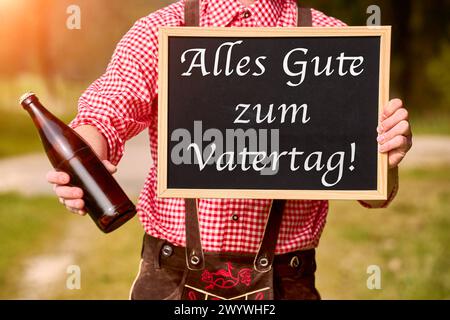 Bavière, Allemagne - 7 avril 2024 : un jeune homme en costume traditionnel bavarois tient une bouteille de bière et une pancarte avec l'inscription : bonne fête des pères salutations pour la fête des pères. PHOTOMONTAGE *** Ein Junger Mann in bayerischer Tracht hält eine Bierflasche und ein Schild mit Aufschrift : Alles Gute zum Vatertag Vatertagsgruß. FOTOMONTAGE Banque D'Images