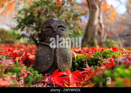 Une statue de Jizo au visage souriant est assise sur un tas de feuilles rouges. La statue est entourée d'un paysage d'automne coloré, temple Enkoji, Kyoto, J Banque D'Images