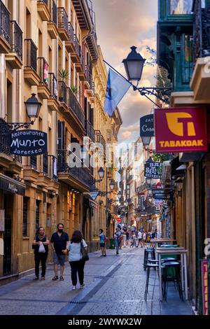 Turistas paseando en la parte Vieja, Donostia, San Sebastián, Gipuzkoa, País Vasco, España, Europa, Adentrarse en la parte Vieja es conocer el verdadero centro social de Donostia, sus calles empedradas como la del 31 de Agosto, que conmemora el incendio ese día de 1813, están llenas de bares para disfrutar de los mejores pintxos de la ciudad, y sus edificios emblemáticos como la Basílica de Santa María del Coro y la iglesia de San Vicente son de gran atractivo e interés,. Banque D'Images