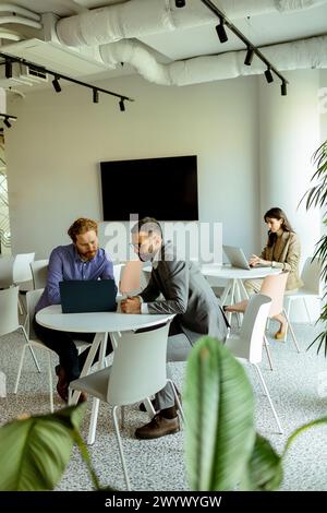 Deux hommes s'engagent dans une conversation animée à une table tandis qu'une femme travaille indépendamment en arrière-plan Banque D'Images