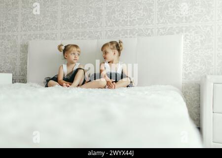 Deux jeunes filles sont assises sur un lit blanc, plongées dans la conversation ou le jeu. Elles sont entourées d'oreillers et de couvertures. Banque D'Images