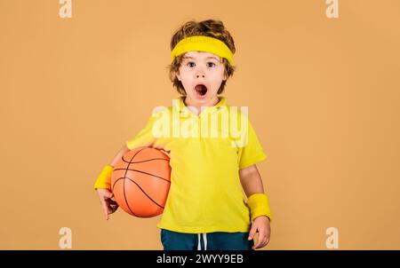 Sport pour enfants. Garçon de joueur de basket-ball surpris en vêtements de sport avec ballon de basket-ball. Fitness, entraînement, style de vie sain et concept de sport de loisir Banque D'Images