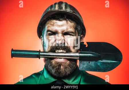 Exploitation minière, industrie lourde et concept de construction. Ouvrier industriel, mineur dans le casque de sécurité avec pelle dans les dents. Homme barbu en colère au travail Banque D'Images