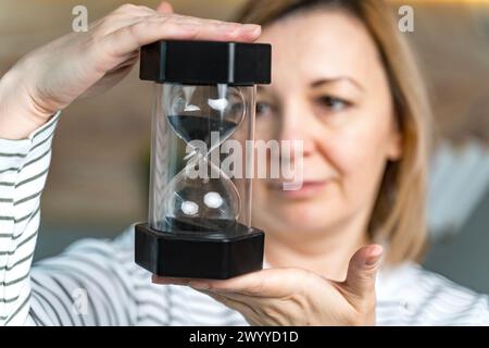 Une femme tient un sablier devant elle, le regarde. Concept de temps qui passe. Foyer sélectionné. Photo de haute qualité Banque D'Images