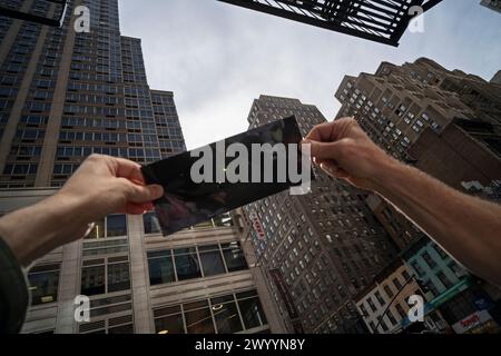 New York, New York, États-Unis 8 avril 2024 Lune passant devant le soleil vu à travers le filtre en plastique dans Midtown Manhattan pendant l'éclipse qui a produit environ 90% de la totalité dans la région de New York Banque D'Images