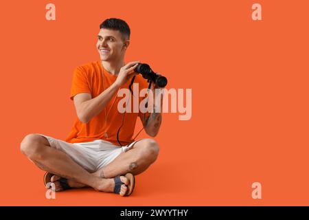 Sauveteur masculin avec des jumelles assis sur fond orange Banque D'Images