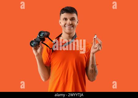 Sauveteur masculin avec jumelles et sifflet sur fond orange Banque D'Images