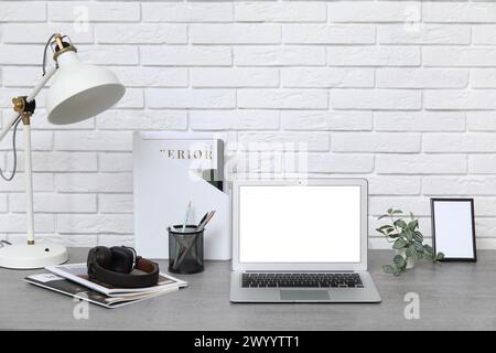 Lieu de travail élégant avec ordinateur portable moderne, lampe et papeterie près du mur de briques blanches Banque D'Images